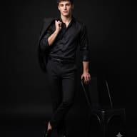Man in Black Fashion with Chair Portrait AI Photo Editing Prompt. AI generated photorealistic studio portrait of a stylish man wearing all black, holding a jacket over his shoulder while leaning on a minimalist metal chair against a dark background.