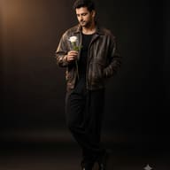 Indian Man in leather jacket with white rose AI Photo Editing Prompt. AI generated cinematic studio portrait of a handsome man in a vintage brown leather jacket and black outfit looking down at a single white rose in moody lighting.   