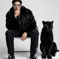 Man in Fur Coat with Black Panther AI Photo Editing Prompt. AI generated high-fashion studio portrait of a man in a black fur coat and silver sunglasses sitting beside a black panther.