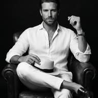 Man in White Linen on Leather Chair AI Photo Editing Prompt. AI generated monochrome studio portrait of a man in white linen attire sitting in a leather armchair and holding a fedora.